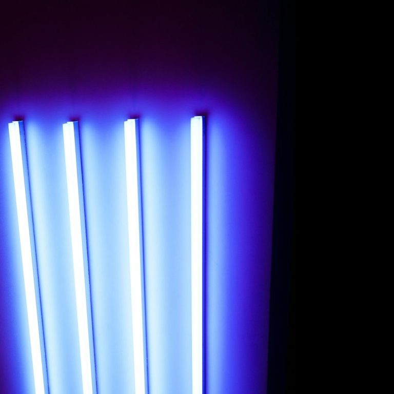 Vier leuchtende blaue Neonröhren an einer dunklen Wand.