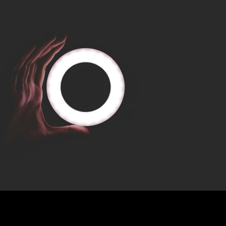 Eine Hand hält einen leuchtenden, runden Ring auf dunklem Hintergrund.