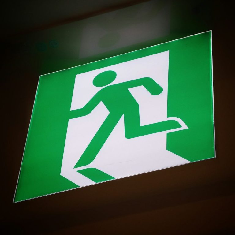 Grünes Schild mit einem stilisierten Menschen, der nach draußen rennt, Hinweis auf Fluchtweg.