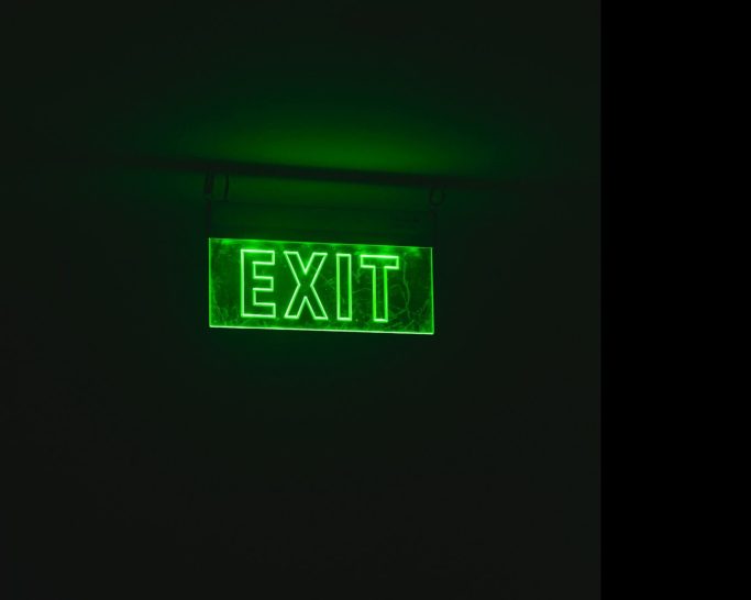 Grünes leuchtendesEXIT-Schild an einer dunklen Wand.