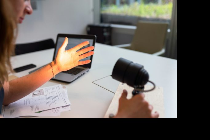 Eine Hand wird von einer Lampe beleuchtet, während ein Laptop im Hintergrund sichtbar ist.